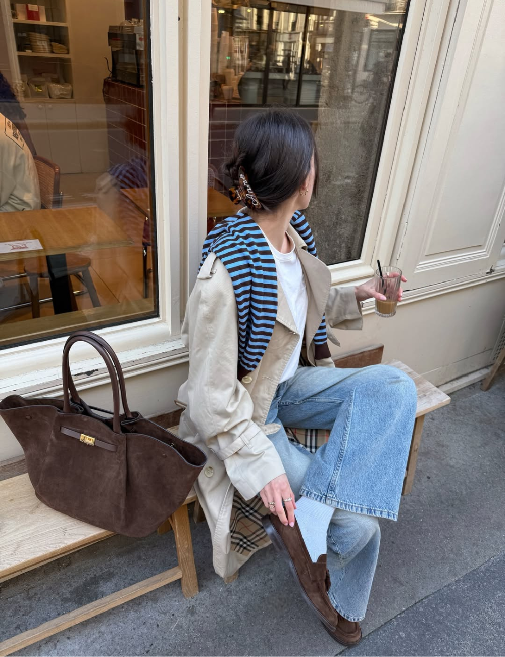 Tendência clássica: modelo posa de trench bege, jeans amplo e mocassim marrom em café, com clima elegante e sereno.