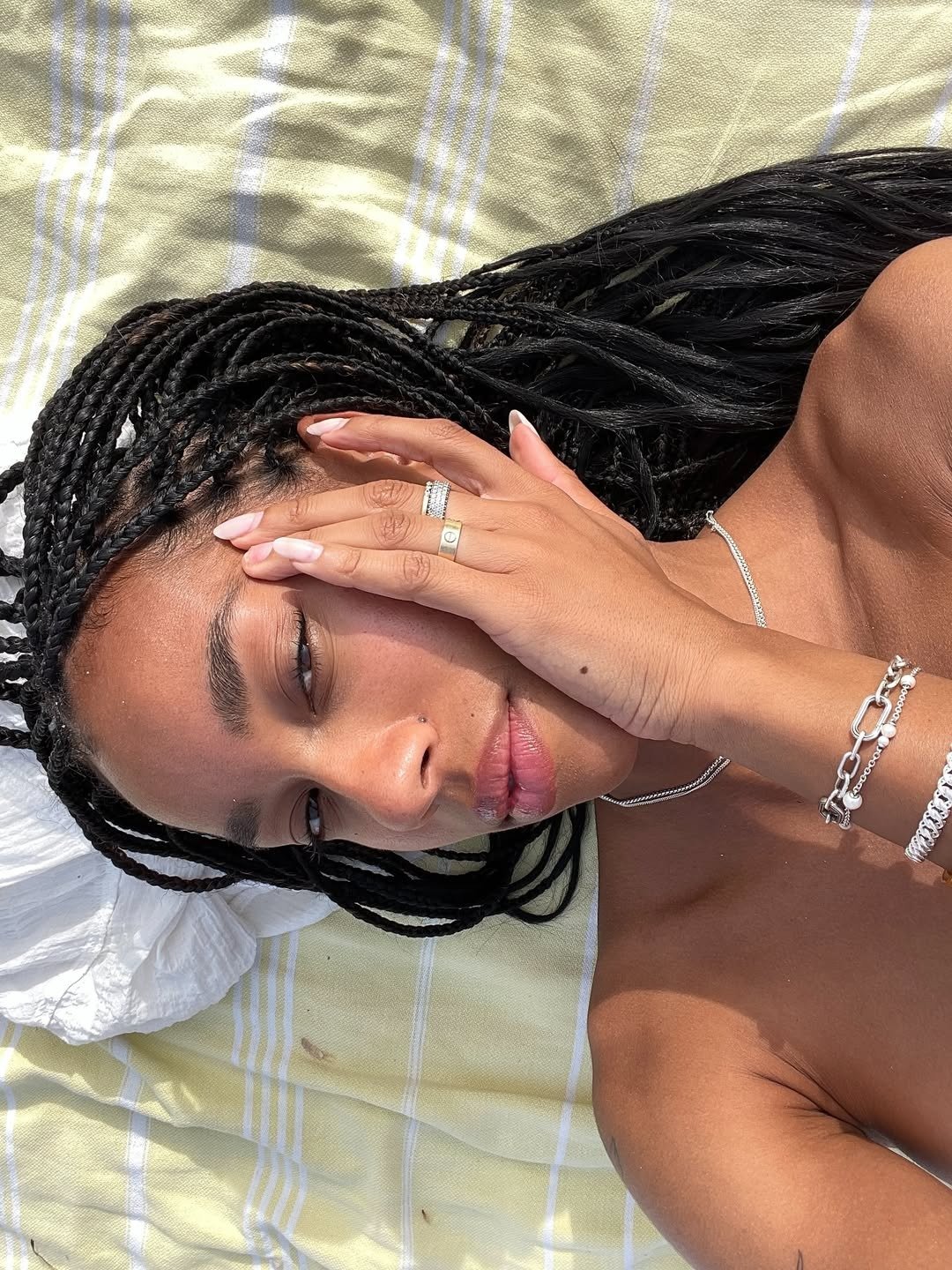 Close destaca sobrancelhas cheias tipo transplante de sobrancelha, tranças negras e joias prateadas ao sol sereno.