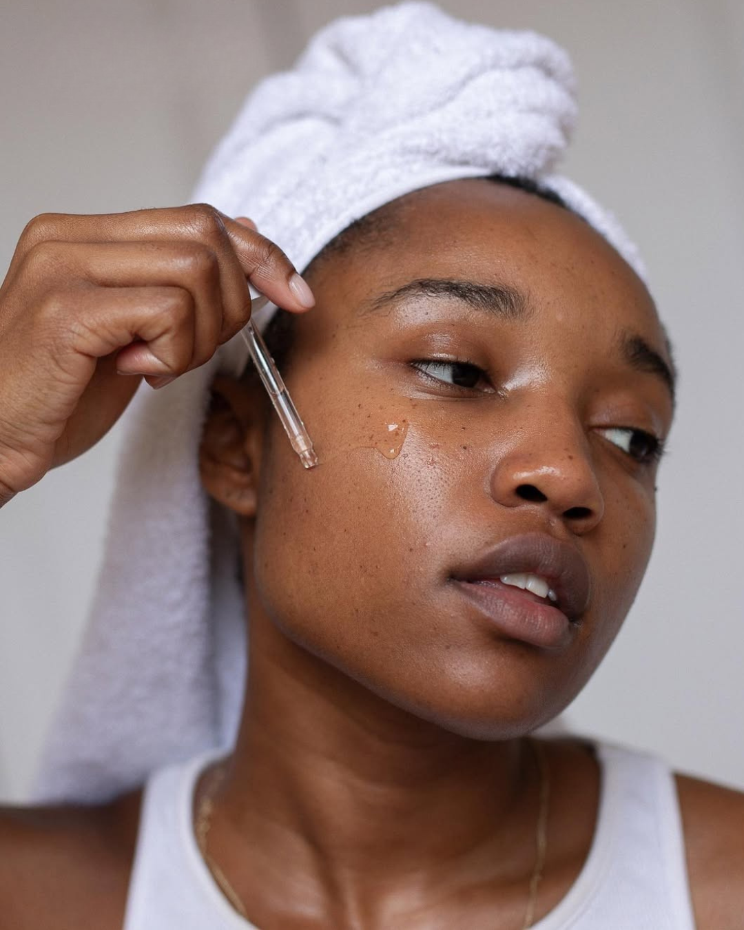 Ácido mandélico para que serve: modelo aplica sérum com conta-gotas no rosto, toalha branca e clima de autocuidado.