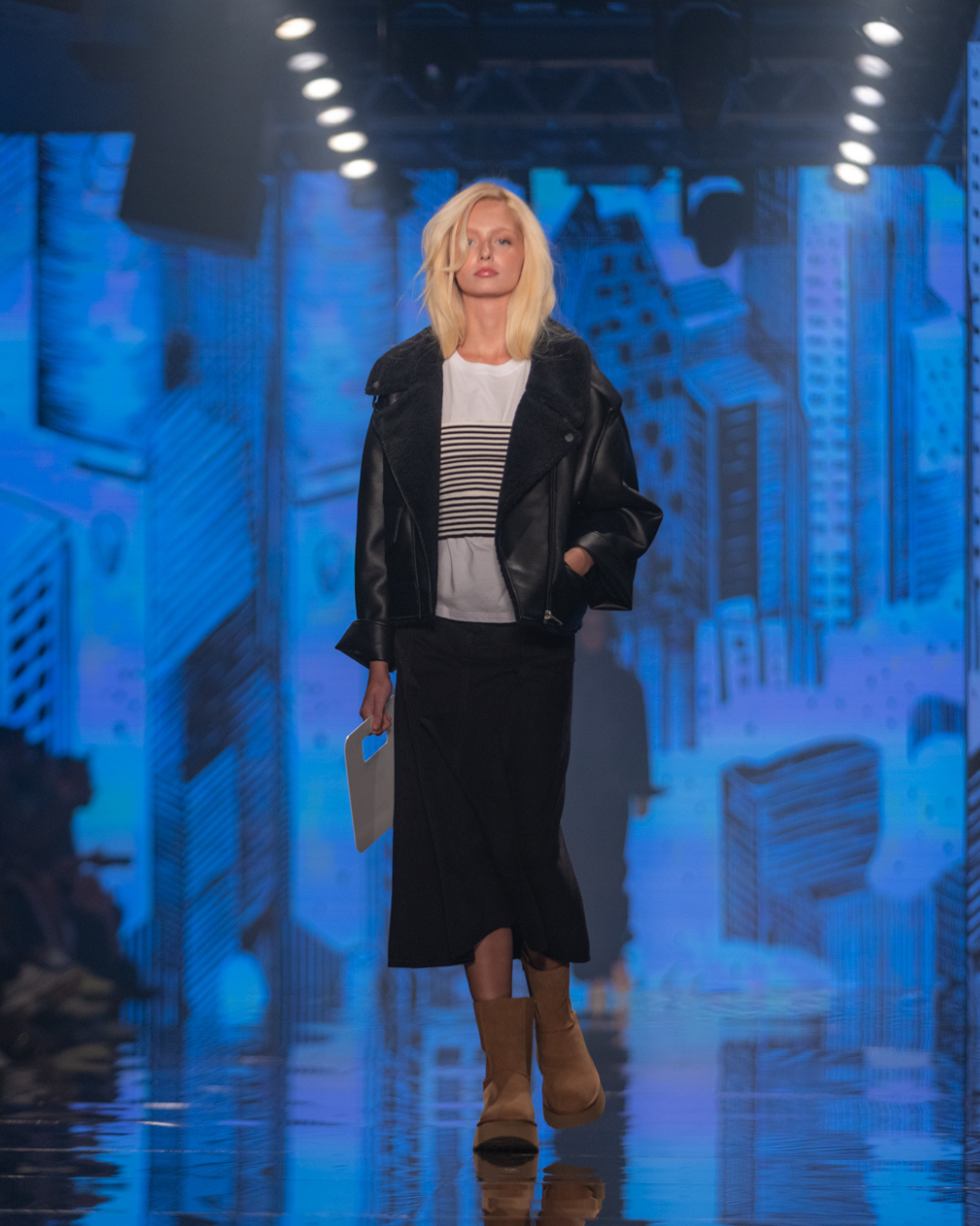 Modelo posa na passarela com jaqueta preta oversized, listras e bota camel, cores e estampas tendência do outono inverno 2026