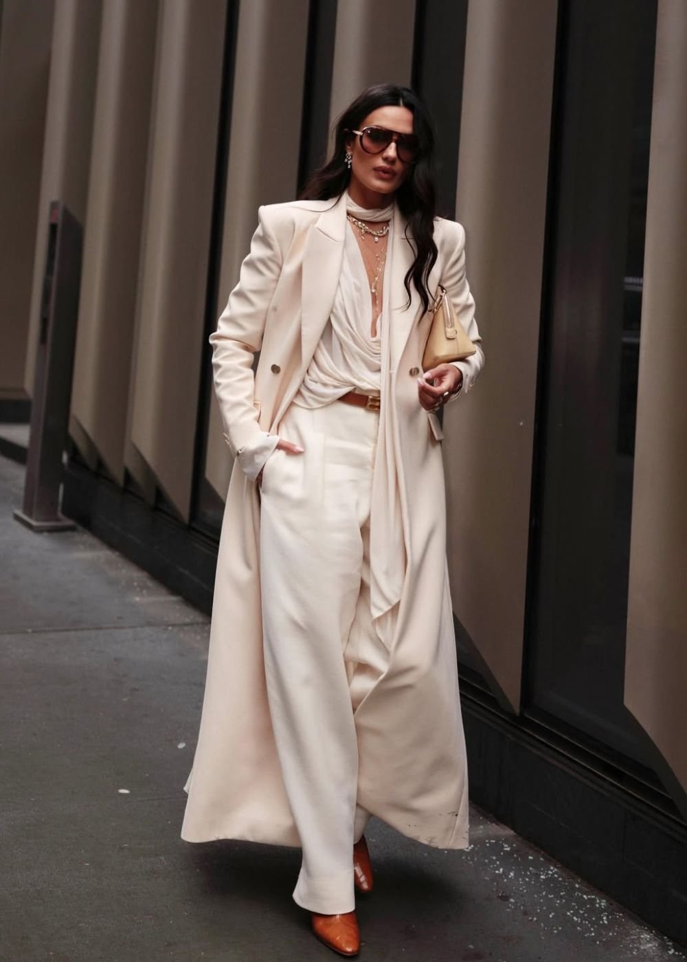 Woman in a cream long blazer coat, draped white blouse, and cream wide-leg trousers