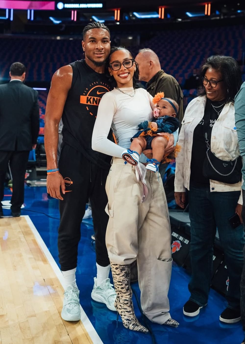 Casal posa na quadra com look esportivo e utilitário em preto, bege e laranja; Texto: KNICKS
