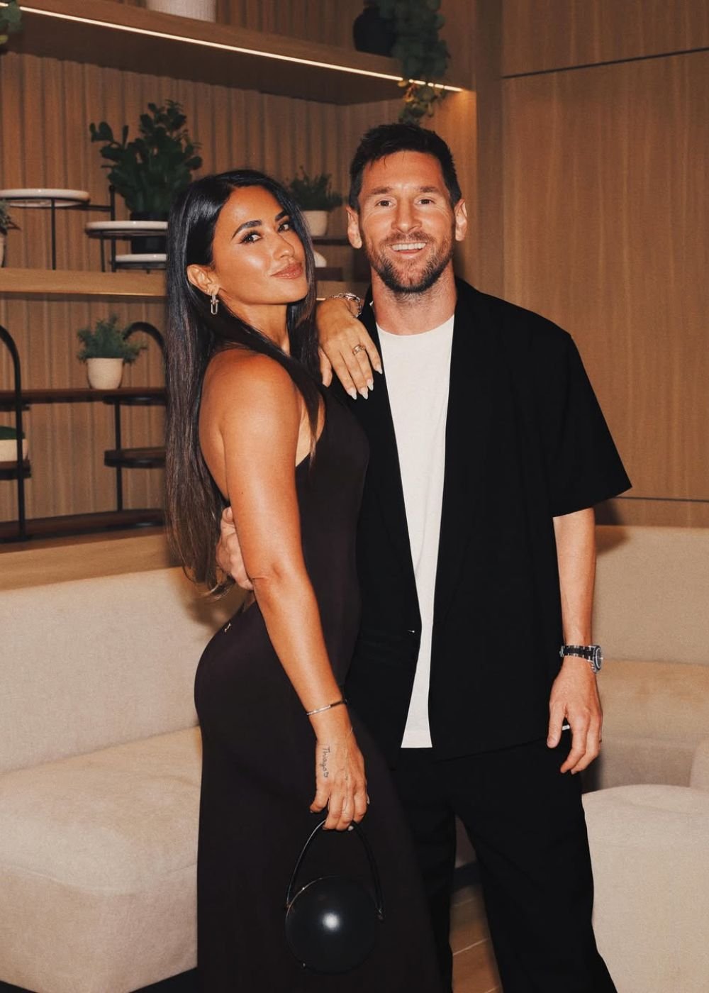 Casal posa elegante em preto e branco, vestido ajustado e alfaiataria leve em ambiente amadeirado; Afinal, o que é WAG?