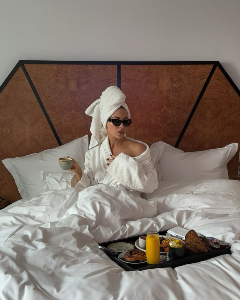 Descubra o que é bom para pele ressecada no dia a dia com modelo de roupão branco, toalha e café na cama acolhedora.