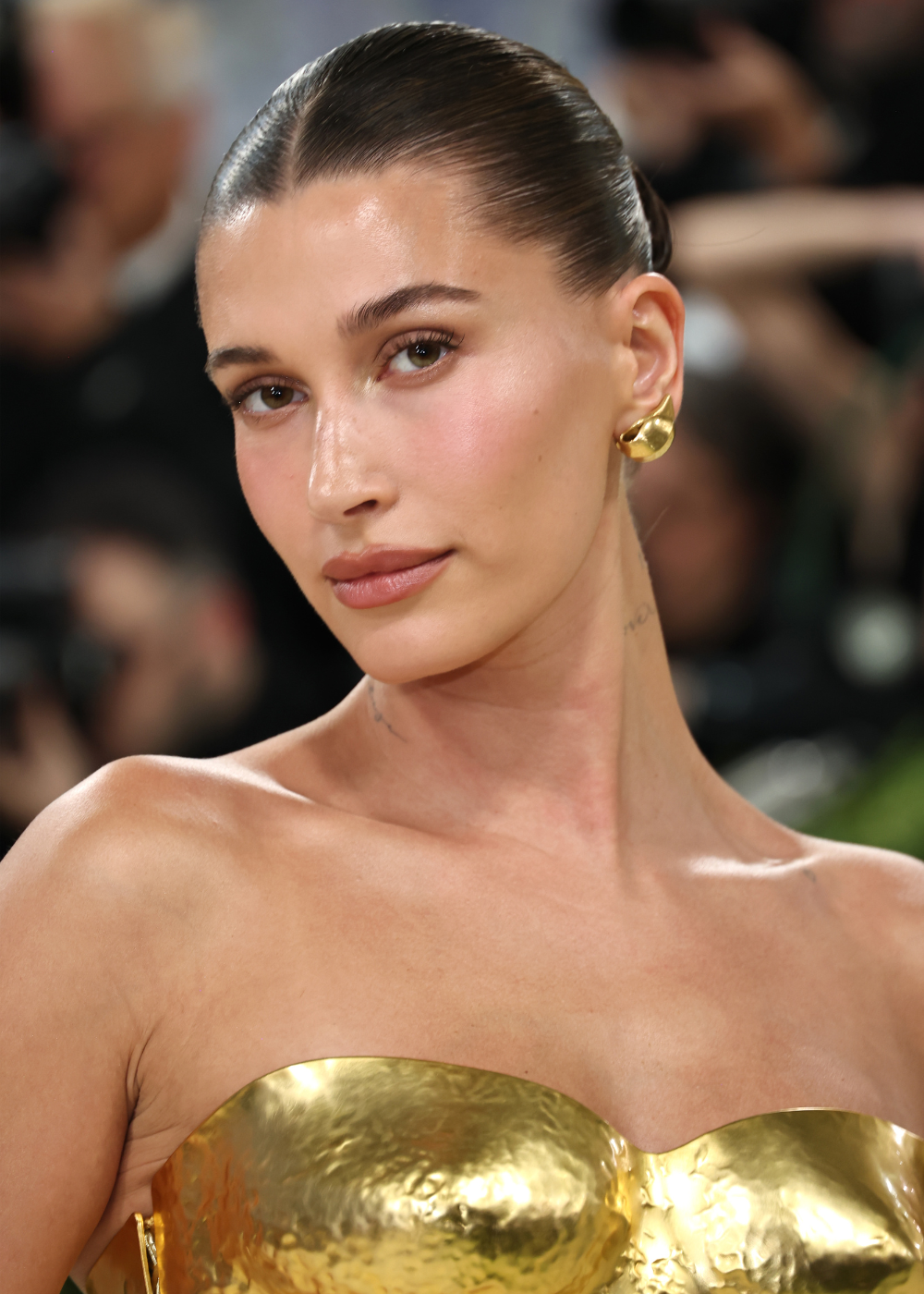 Maquiagem dos anos 90 inspira modelo posa com pele glow, blush rosado, coque polido e vestido dourado metálico elegante