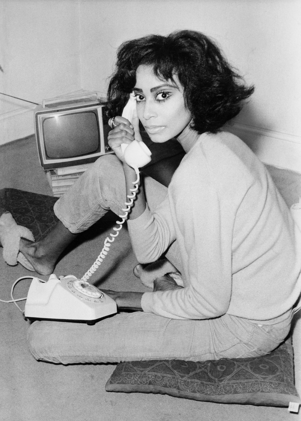 Maquiagem dos anos 60 em preto e branco: modelo posa ao telefone com delineado marcante, tricô leve e jeans, clima retrô